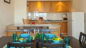 A compact kitchen with wooden cabinets, a microwave, and a small island with chairs. - Charming 1-bedroom apartment in Portimão (Portimão)