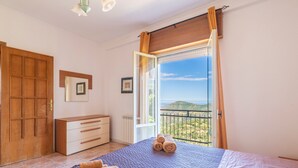 A bedroom with a bed, a dresser, a door, and a balcony with a view.