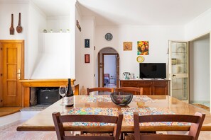 Un coin repas avec une table en bois, des chaises, une bouteille de vin et un téléviseur en arrière-plan.