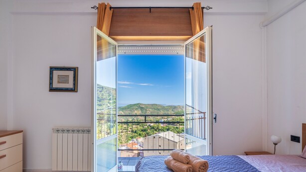 A bedroom with a large window, a bed with rolled towels, a radiator, and a framed picture on the wall.