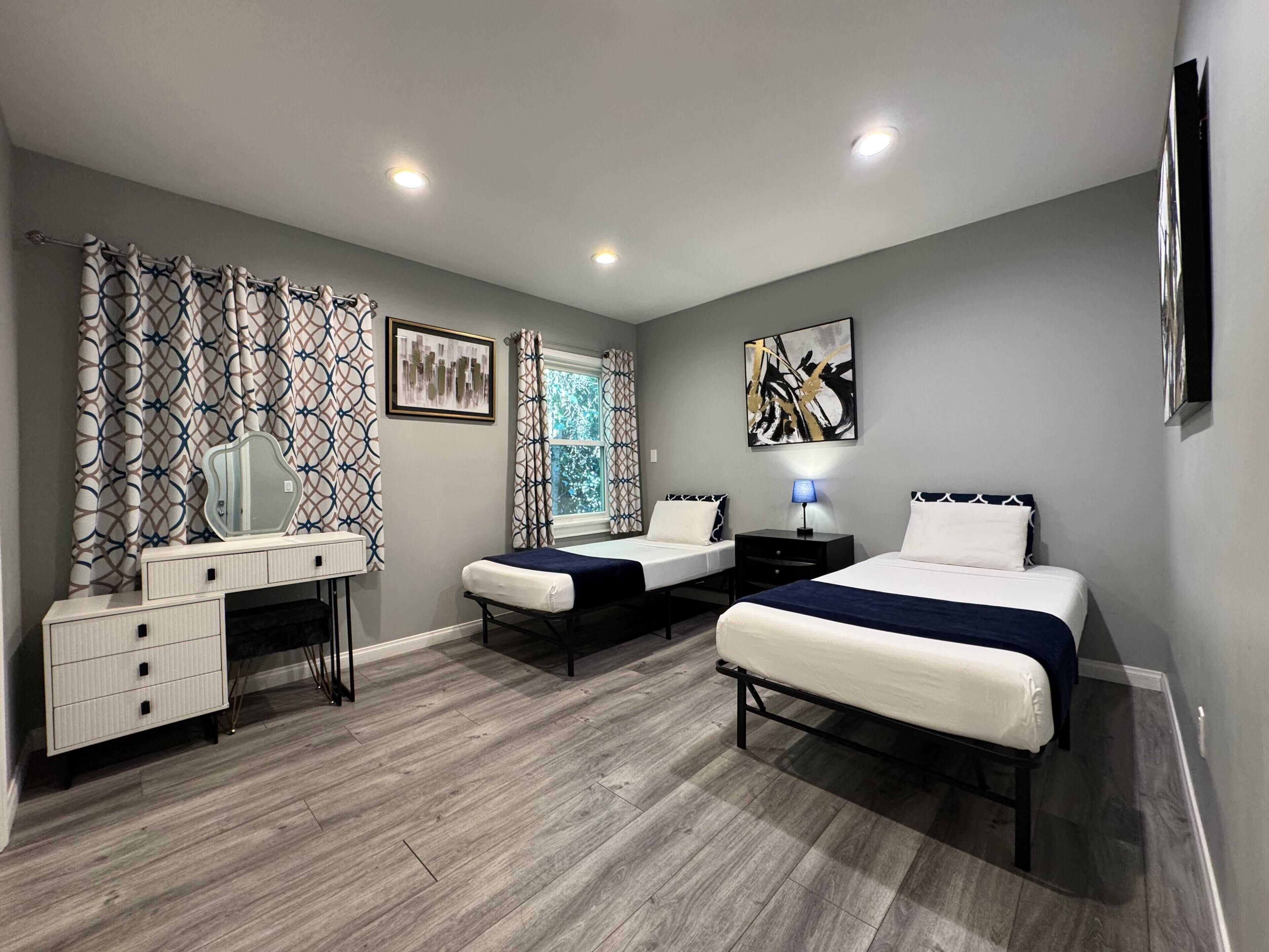 Une chambre avec deux lits, une commode, un miroir et des œuvres d’art accrochées aux murs.