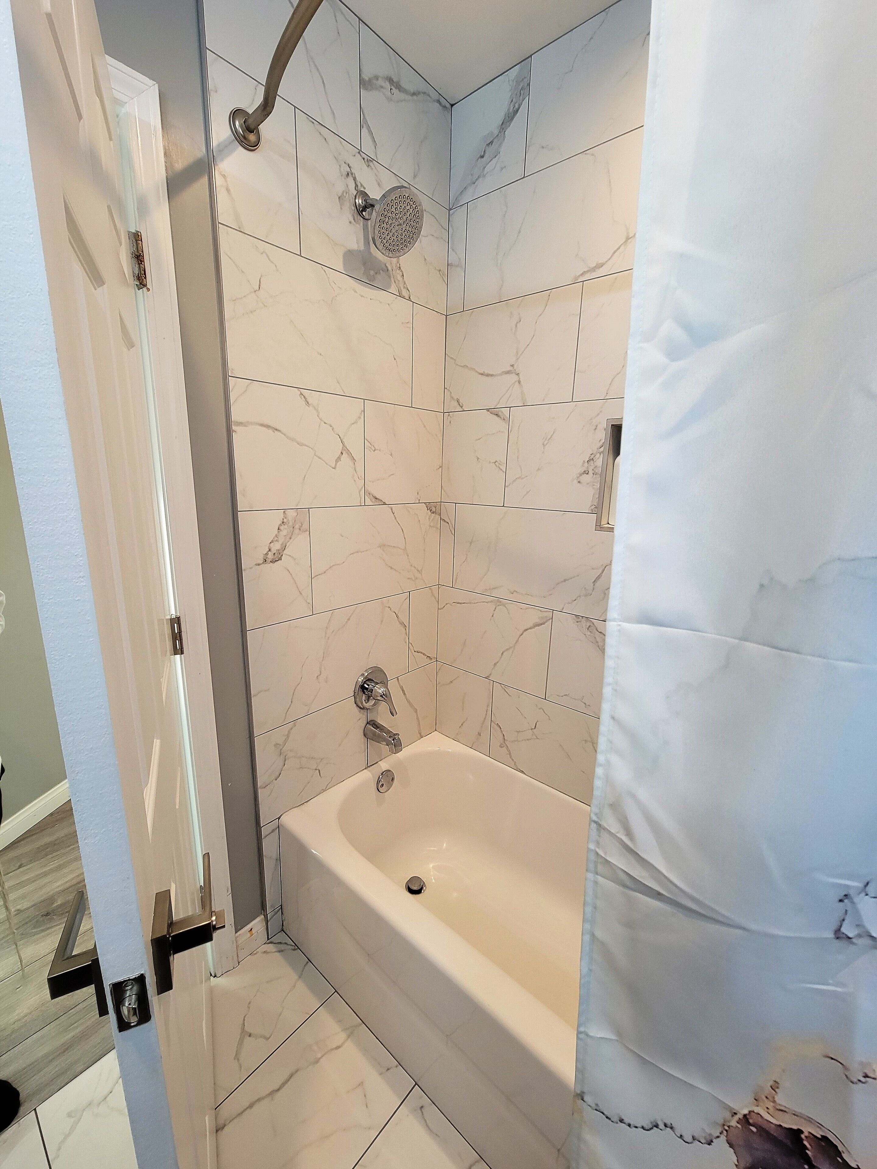 A bathroom with a bathtub, a showerhead, and a door with a handle.