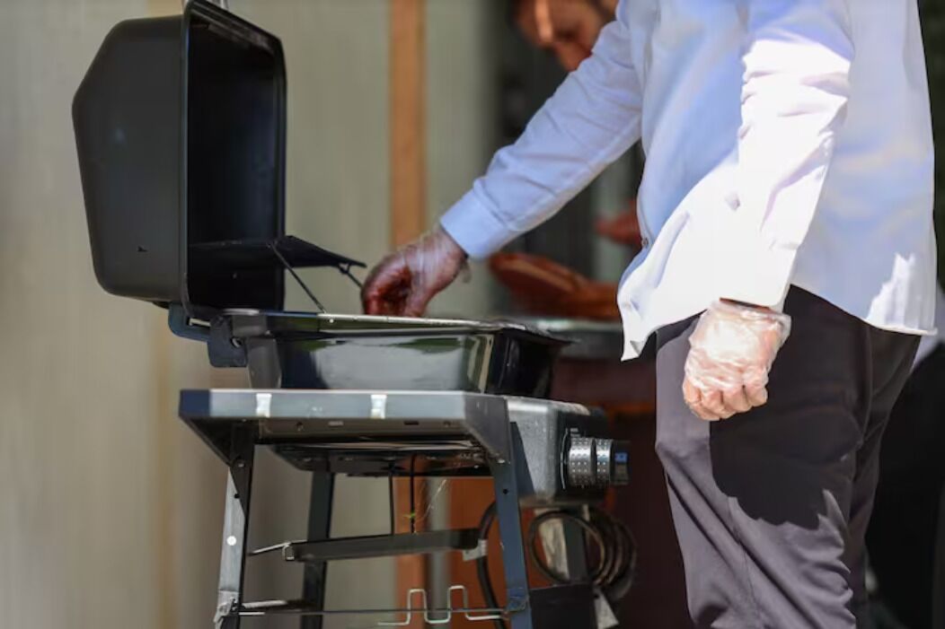 A person in a white shirt and black pants operating a portable grill.
