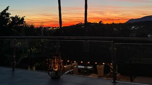 A terrace with a view of a sunset, a decorative light fixture, and a dining area with tables and chairs.