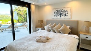 A bedroom with a large bed, a view of a pool and lounge chairs, and a tree artwork on the wall.