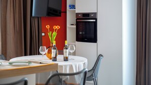 A dining area with a table set for two, a television mounted on the wall, and a modern oven. - Kymè - One Bedroom Apartment, Sleeps 4 (NOTO)