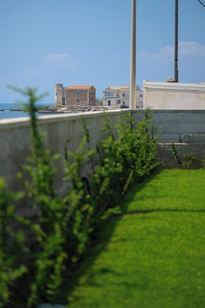 A coastal building with a view of the sea, a concrete wall, and some greenery in the foreground.