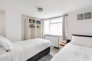 A hotel room with two beds, a wardrobe, a window with curtains, and a nightstand. - Cosy Central Home with Private Garden & Fast Wifi, Comfy 3BR Home • Contractor Friendly • Town Centr... (Colchester)