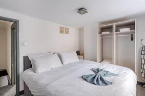 A neatly made bed with white linens and a blue towel, a wardrobe with hanging space, and a small bedside table with a lamp. - Cosy Central Home with Private Garden & Fast Wifi, Comfy 3BR Home • Contractor Friendly • Town Centr... (Colchester)