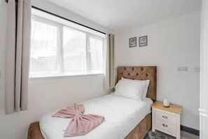 A neatly made bed with a pink towel, a wooden headboard, and a small bedside table with a cup. - Cosy Central Home with Private Garden & Fast Wifi, Comfy 3BR Home • Contractor Friendly • Town Centr... (Colchester)
