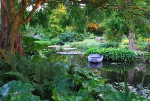 A serene garden with a pond, lush greenery, and a wooden boat. - Cosy Central Home with Private Garden & Fast Wifi, Comfy 3BR Home • Contractor Friendly • Town Centr... (Colchester)