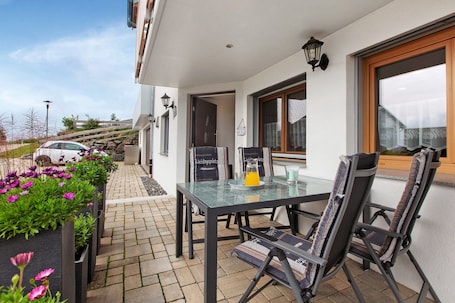 A patio with a table and chairs, a car parked outside, and a building with a window and a door.. Apartment 'Morgensonne' with Mountain View, Private Terrace and Wi-Fi