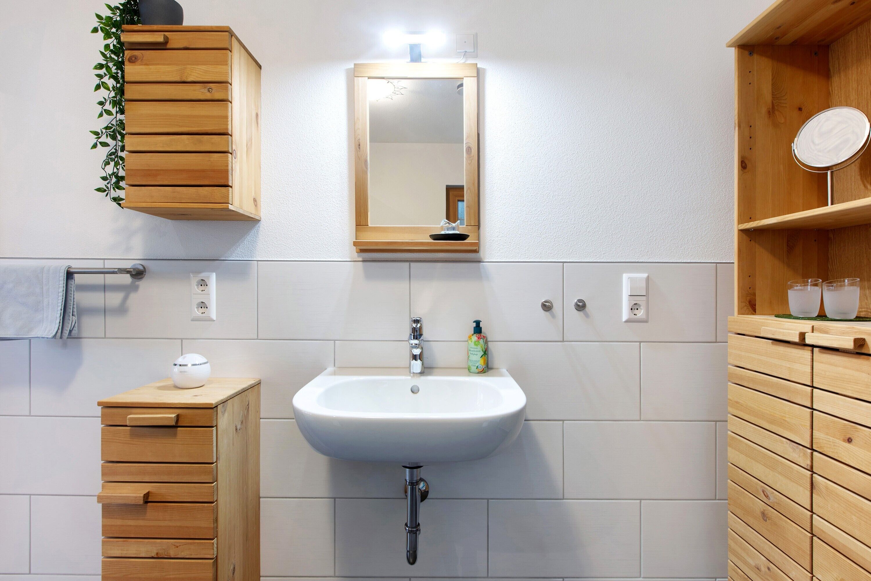 A bathroom with a wooden cabinet, a sink, a mirror, and a small shelf with a round mirror.