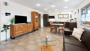 Una sala de estar moderna con una mesa de centro de vidrio, un sofá de cuero marrón, armarios de madera, un televisor de pantalla plana y un comedor con mesa y sillas.