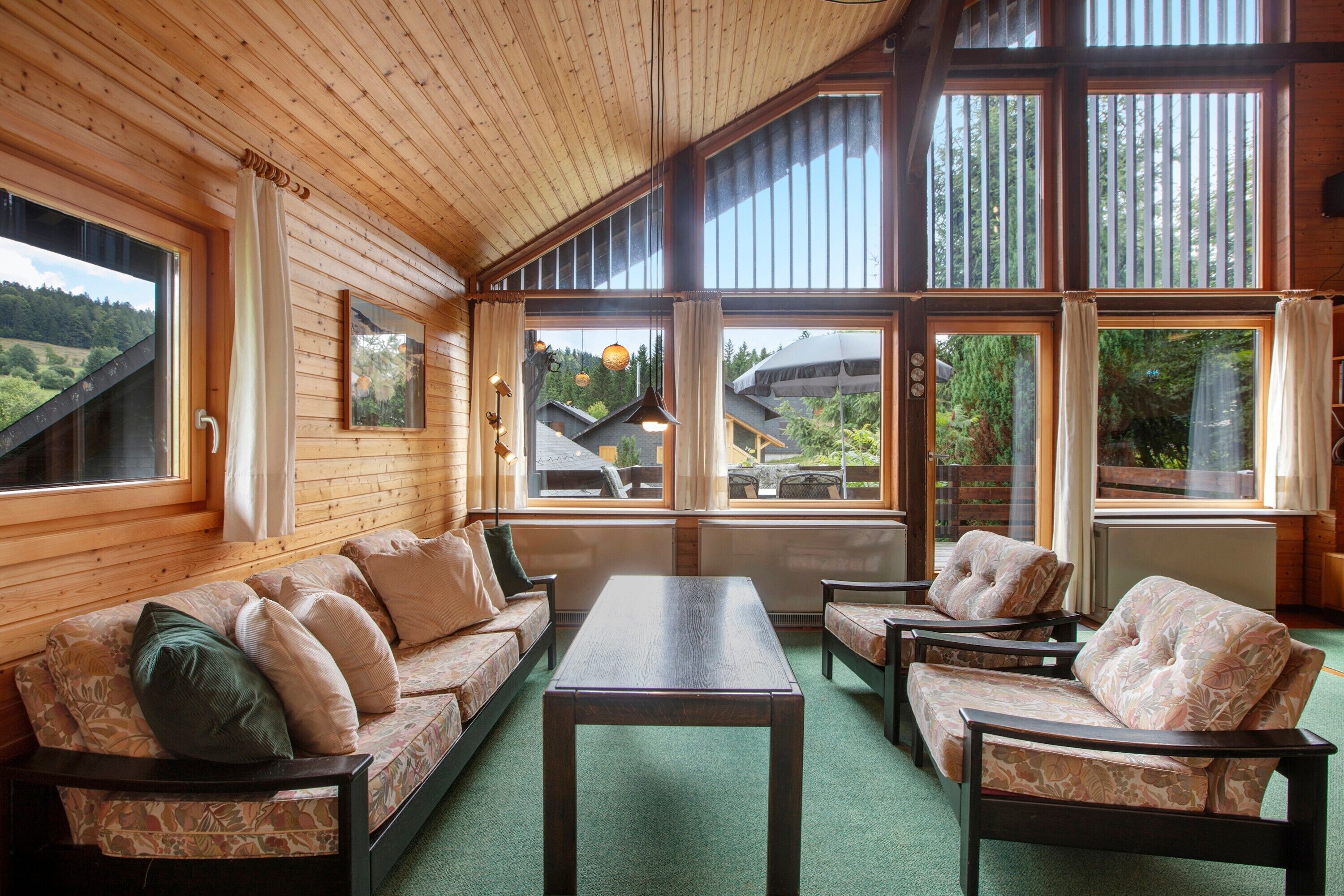 L'intérieur d'un chalet en bois comprend un canapé, des fauteuils, une table et de grandes fenêtres qui offrent une vue sur l'extérieur.