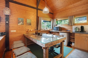 A wooden cabin interior with a kitchen, dining area, and a large window.