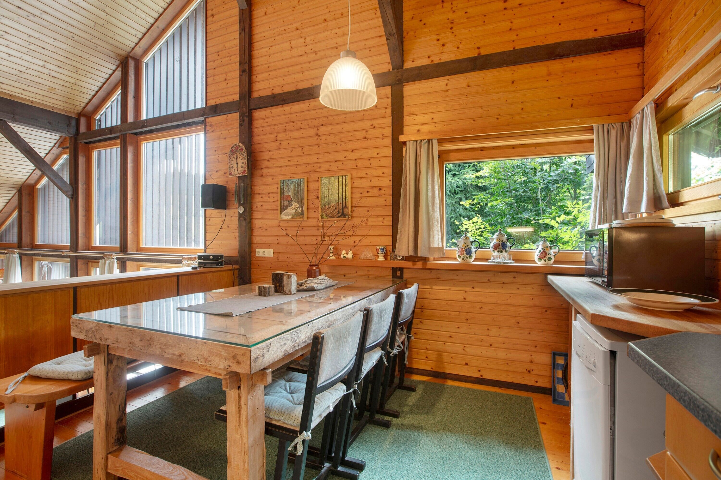 Un intérieur en bois comprenant une table à manger, des chaises, un coin cuisine et de grandes fenêtres.