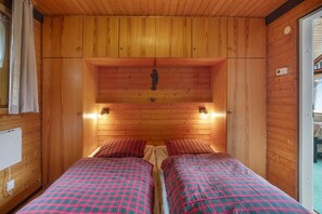 A wooden cabin room with two beds, a wooden ceiling, and a small window.