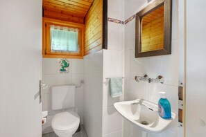 A bathroom with a toilet, sink, mirror, and a window with a curtain.