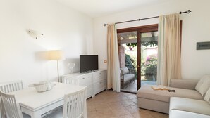 A room with a white table, a TV on a dresser, a sofa, and a sliding glass door leading to an outdoor area. - Casa di Barbara al Mare by Wonderful Italy (Olbia)