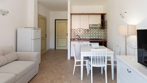 A compact kitchen with white cabinets, a tiled backsplash, and a dining area with white chairs and a table. - Casa di Barbara al Mare by Wonderful Italy (Olbia)