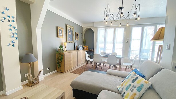 A modern living room with a sofa, dining table, and chairs. There is a chandelier, a lamp, and a cabinet with framed pictures. - At Clém's, 8 people, private garage, wifi + Netflix (Reims)