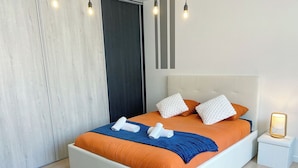 A modern bedroom with a large bed, white headboard, and a bedside table with a lamp. - At Clém's, 8 people, private garage, wifi + Netflix (Reims)