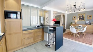 A modern kitchen with wooden cabinets, a built-in microwave, and a dining area with a glass table and white chairs. - At Clém's, 8 people, private garage, wifi + Netflix (Reims)