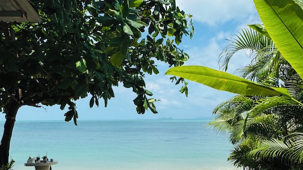A beach with a clear view of the ocean, surrounded by lush greenery and a few outdoor seating areas. - Beachfront Villa with Sunset (Koh Samui)