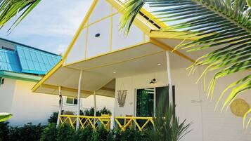 Una casa con techo amarillo, un porche con barandillas amarillas y una pared blanca con una ventana.