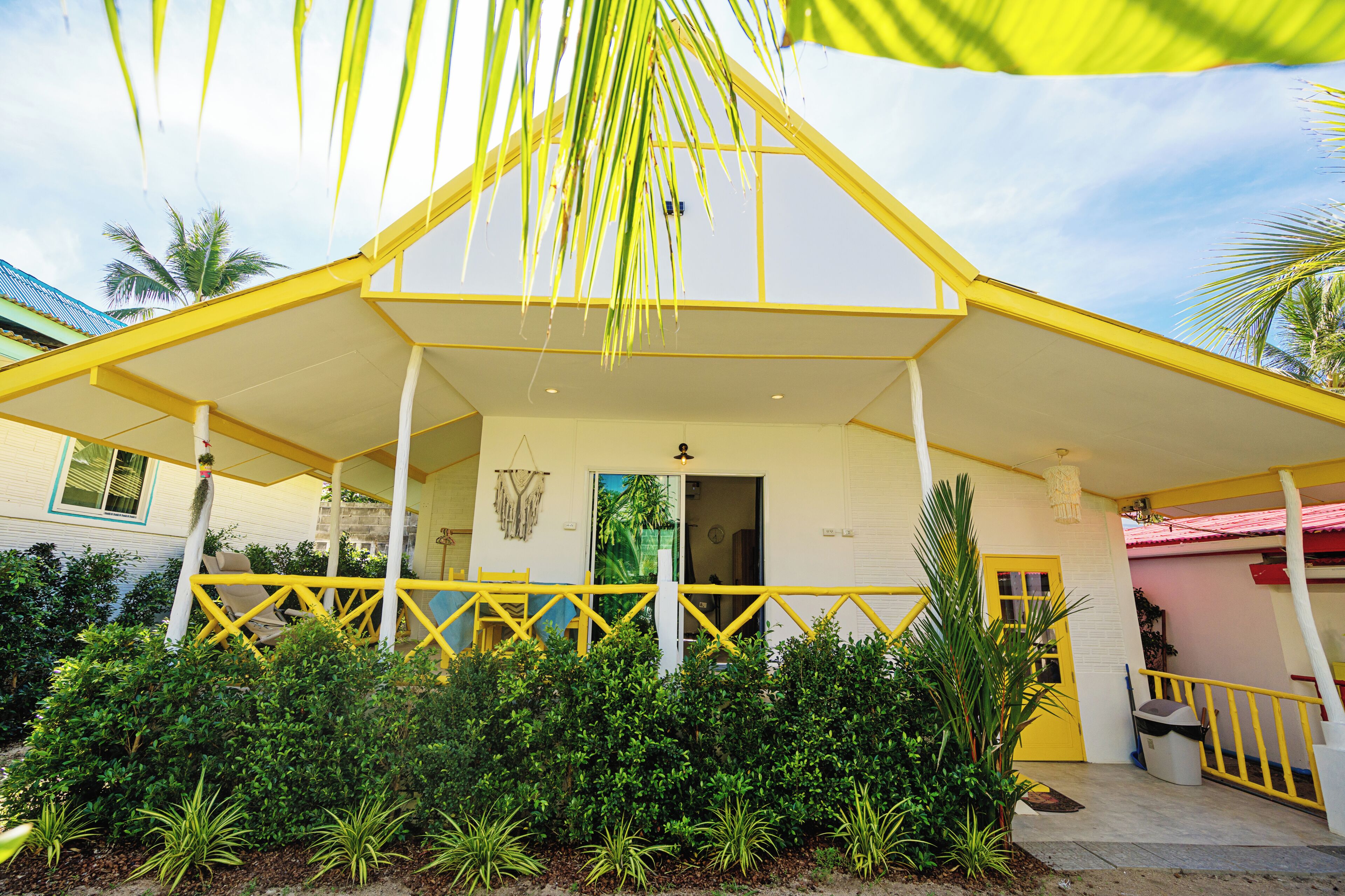 A yellow building with a covered porch, surrounded by greenery.