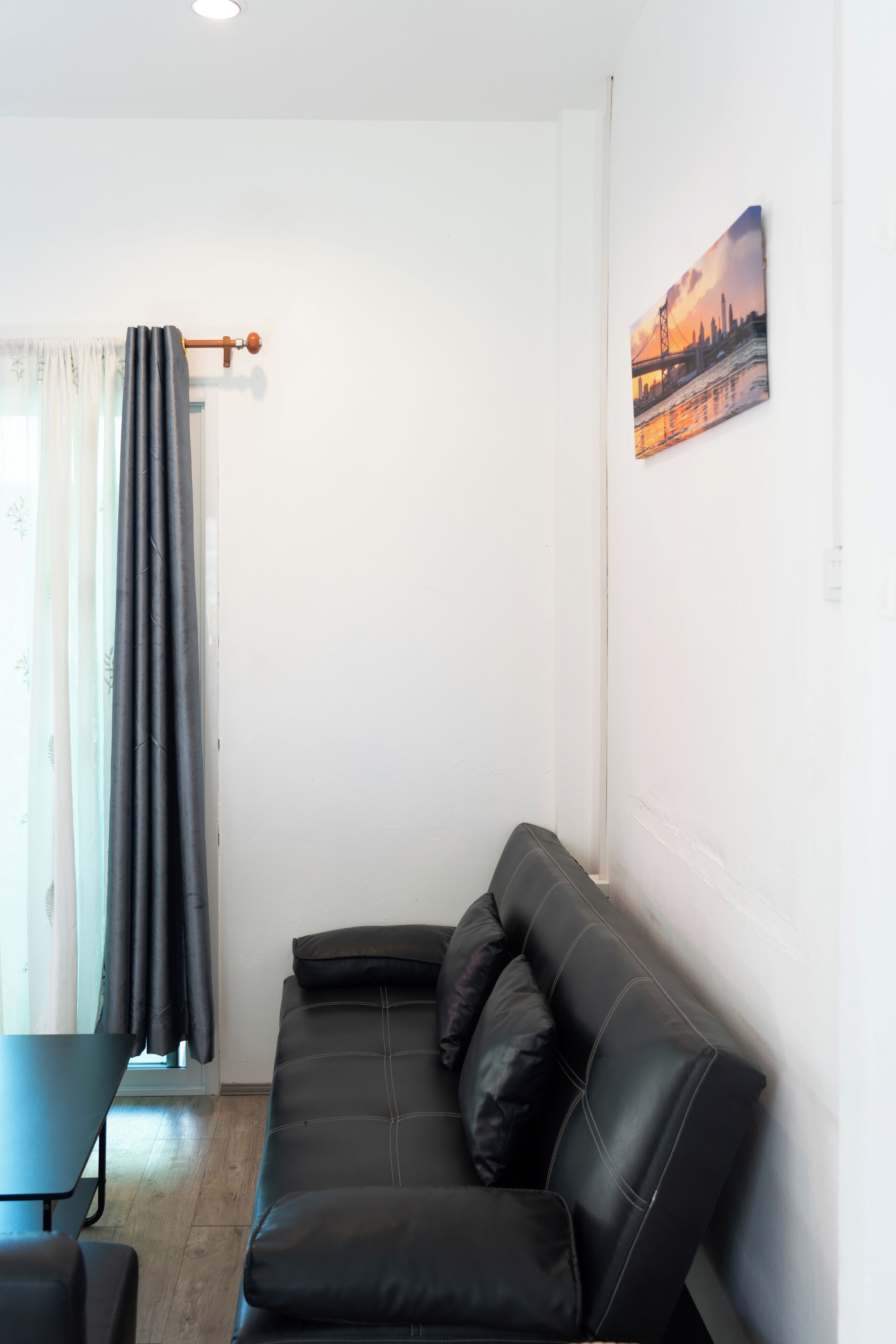 Een woonkamer met een zwarte leren bank, een kleine tafel en een schilderij aan de muur.