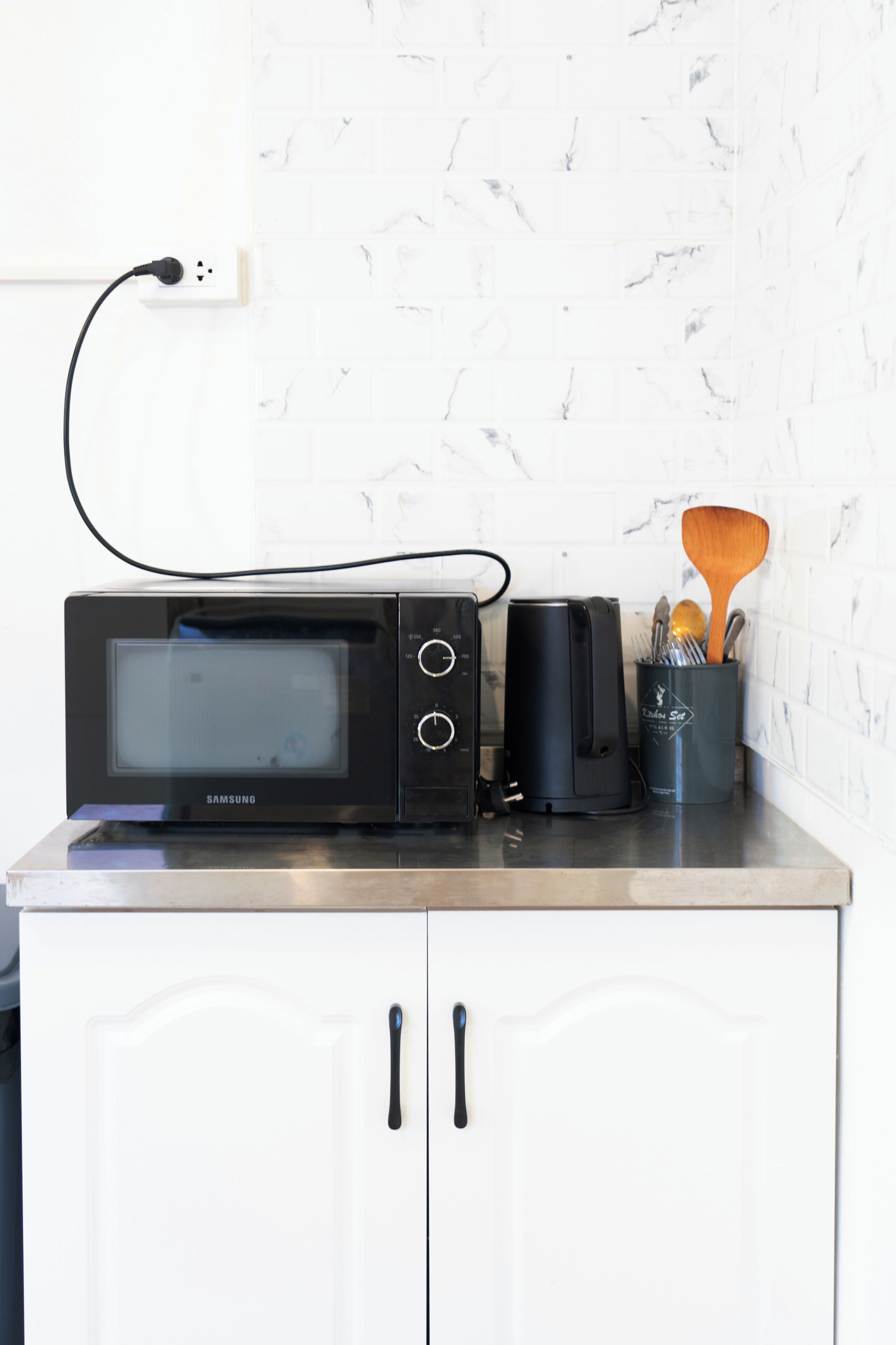 Una cocina con microondas, cafetera y un portalapices sobre la encimera.