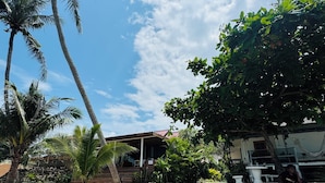A sandy outdoor area with palm trees, a concrete bench, and a building with a red roof in the background. - Beachfront Villa with Sunset (Koh Samui)