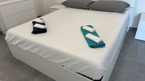 A neatly made bed with white and teal towels, a grey headboard, and a white nightstand.