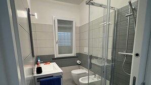 A modern bathroom with a glass shower enclosure, a toilet, and a sink with a towel.