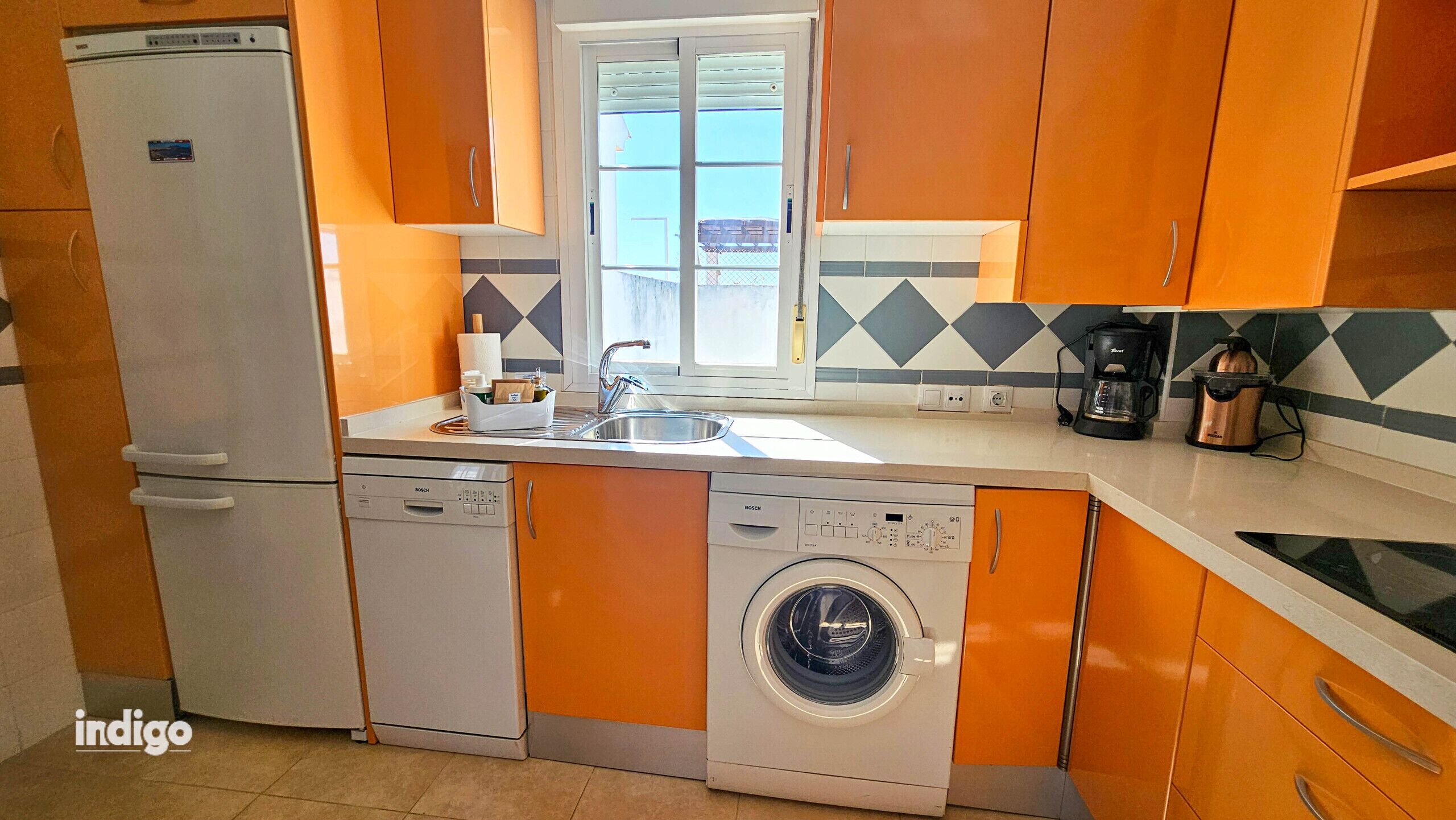 A compact kitchen with a Bosch dishwasher, washing machine, and coffee maker.