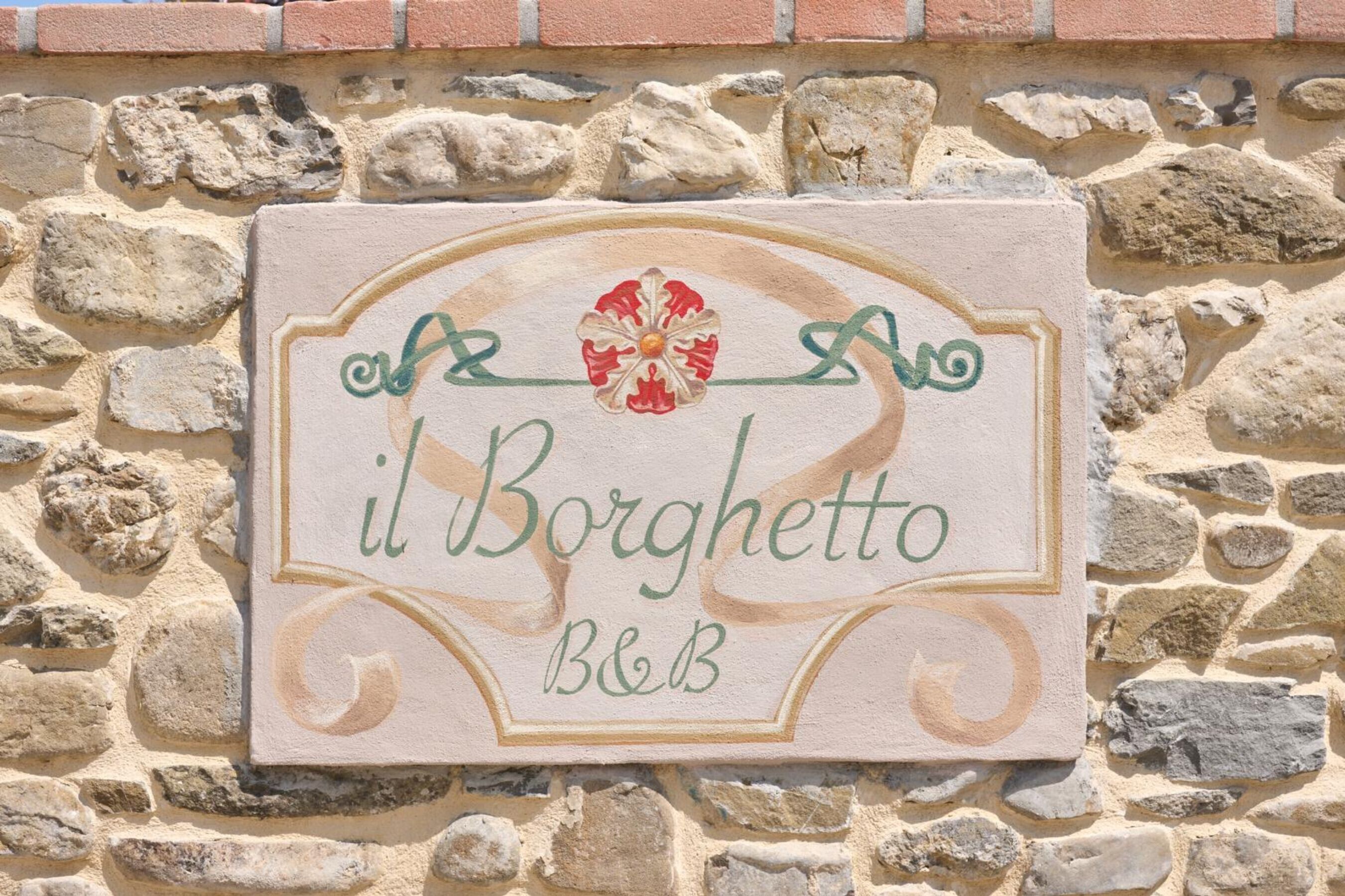 Een stenen muur met een bordje voor 'il Borghetto B&B', voorzien van een decoratief embleem.