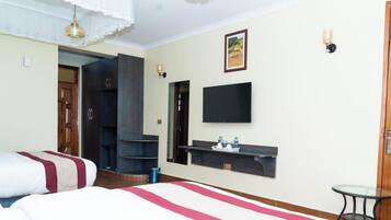 A hotel room with a bed, a TV, a shelf with toiletries, and a door leading to another room.
