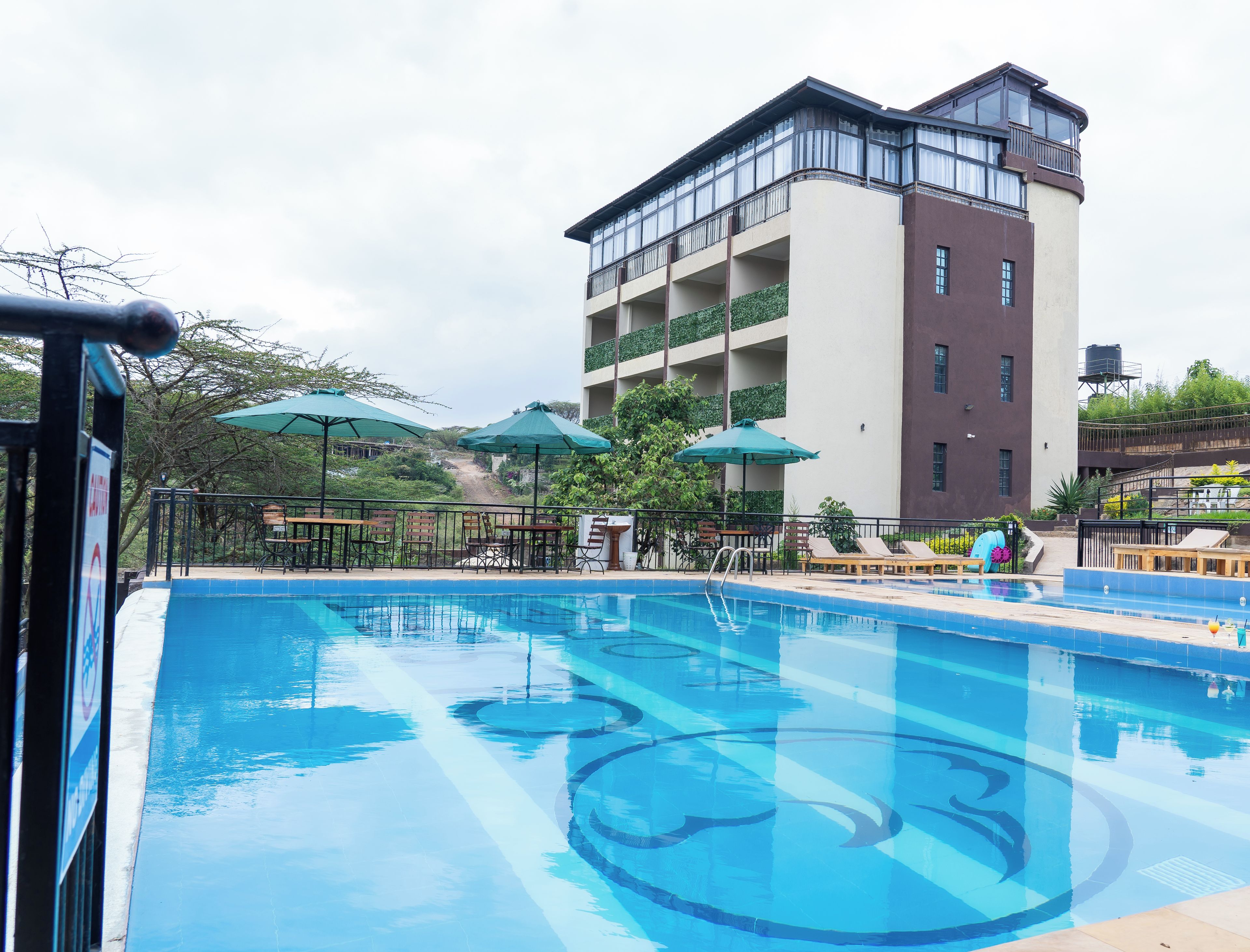 A swimming pool with lounge chairs and umbrellas, surrounded by a building with balconies.