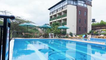 A swimming pool with lounge chairs and umbrellas, surrounded by a building with balconies.