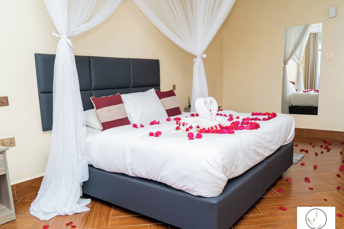 Una cama bien hecha con ropa blanca, almohadas rojas y beige, y un dosel.