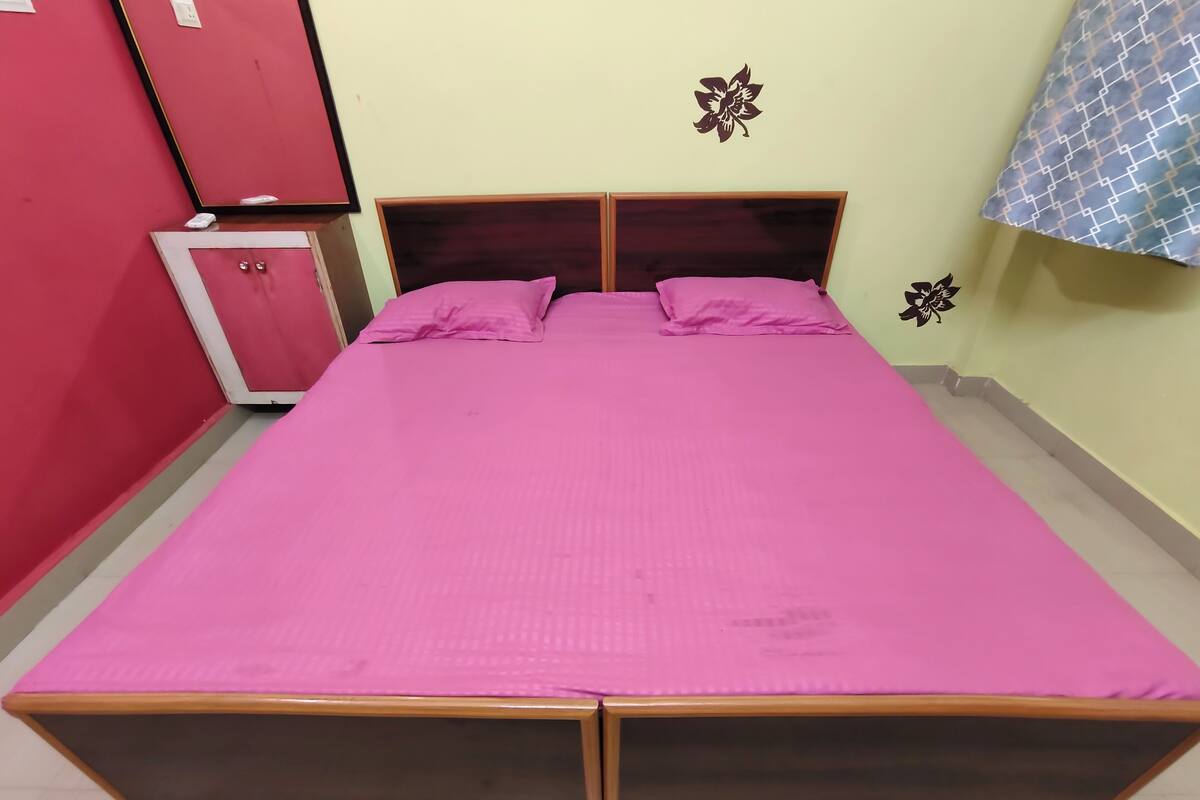 A double bed with a wooden frame and a pink bedspread in a room with a red wardrobe and a wall-mounted flower decoration.
