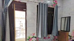 A bedroom with a bed, a wardrobe, a mirror, and a door leading to a balcony. - Gauri Shankar P Guest house (Varanasi)