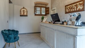 A reception area with a desk, a chair, a window with shutters, a wall-mounted artwork, and a door. - Room 'Il Borghetto Lavanda' with Shared Garden, Wi-Fi and Air Conditioning (Borgo San Lorenzo)