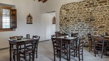 A dining area with wooden tables and chairs, stone walls, and arched niches with sculptures.