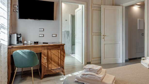 Habitación de hotel con un escritorio de madera, televisión, una silla, una cama y un baño visible a través de una puerta abierta.