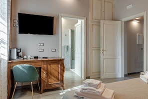 A hotel room with a wooden desk, a television, a chair, a bed, and a bathroom visible through an open door. - Room 'Il Borghetto Orchidea' with Shared Garden, Wi-Fi and Air Conditioning (Borgo San Lorenzo)