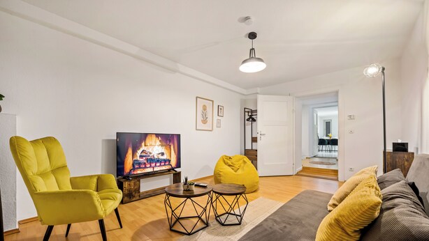 A modern living room with a sofa, a yellow armchair, a TV, and a bean bag. - Cosy&Central, 500m from Main Station, Work&Stay (Wiesbaden)
