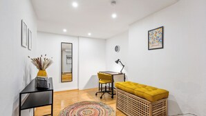 A modern, well-lit room with a wooden floor, a black desk, a yellow chair, a yellow ottoman, a colorful rug, and a wooden basket. - Cosy&Central, 500m from Main Station, Work&Stay (Wiesbaden)